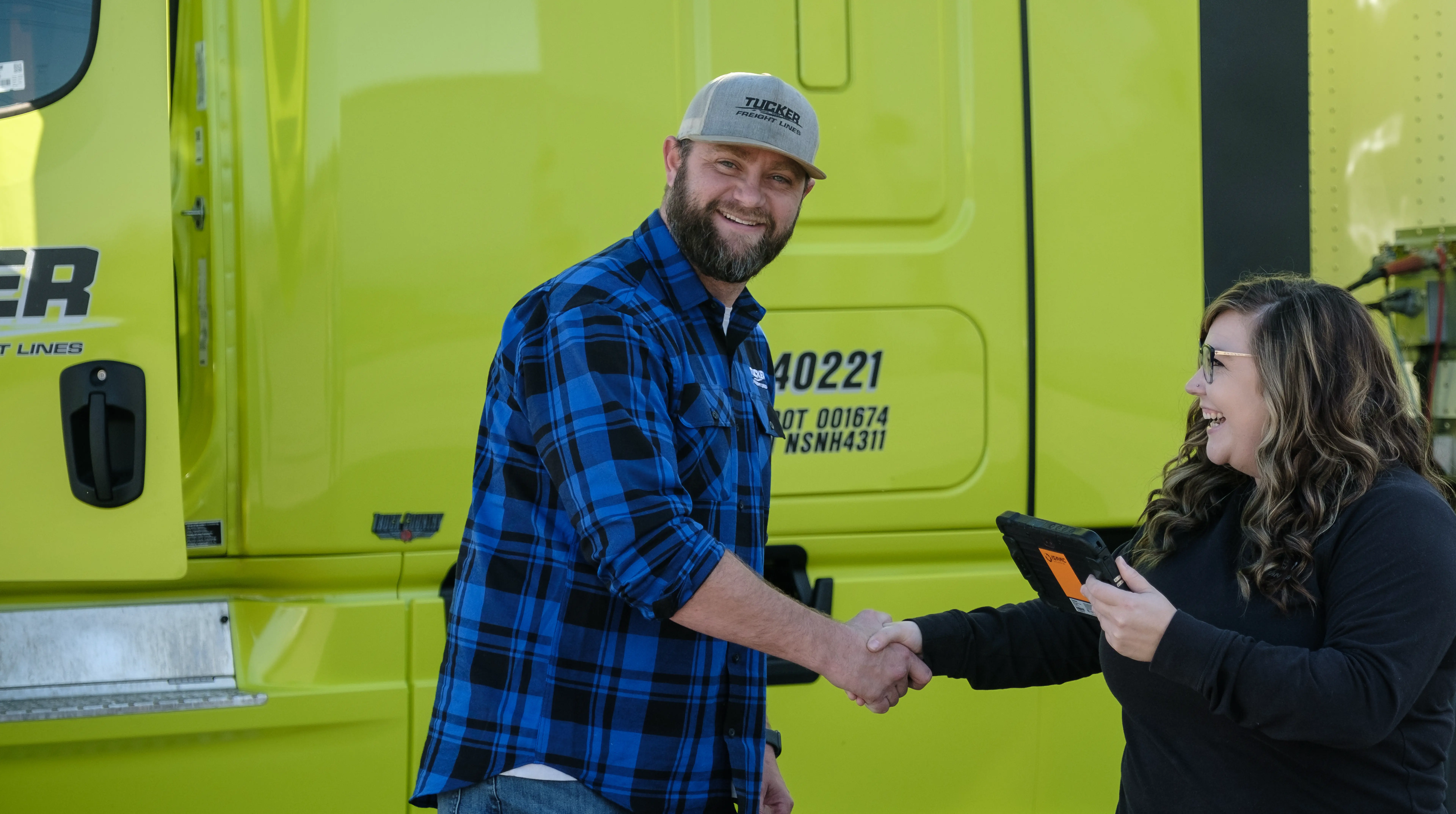 Tucker Freight Lines driver shaking hands with a team member beside a green truck.
