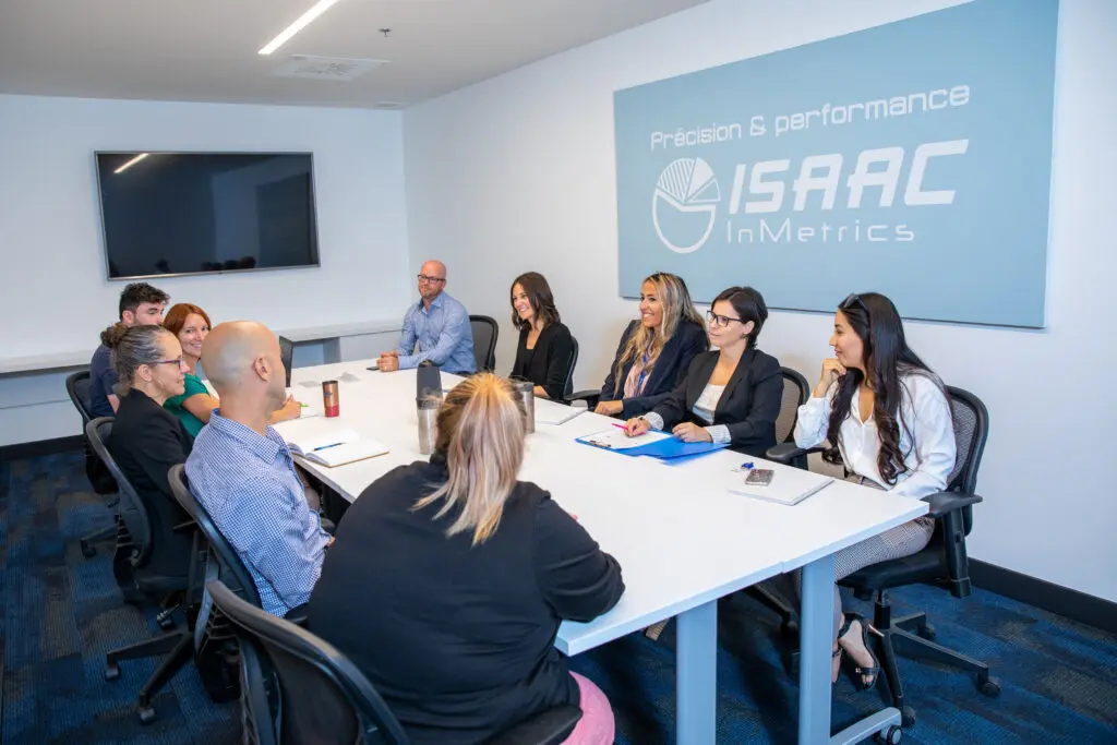 ISAAC team around white table under “Precision & Performance” sign discussing strategy.